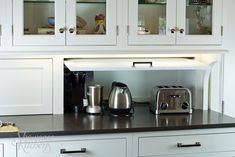 a kitchen with white cabinets and black counter tops, including a toaster and coffee maker