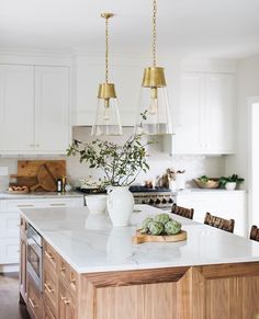 a kitchen with white cabinets and gold pendant lights hanging from the ceiling over the island