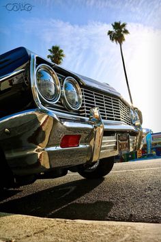 an old car parked on the side of the road with palm trees in the background