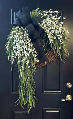 a wreath with white flowers hanging on a black front door, decorated with a bow