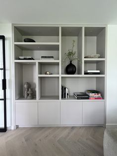 a white bookcase with books and vases on top of it in a living room