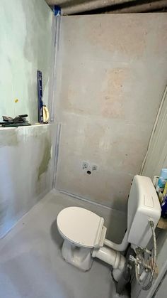 a white toilet sitting inside of a bathroom next to a wall with drywall on it