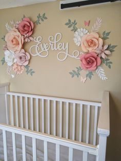 there is a crib in the room with flowers on the wall and name painted on the wall