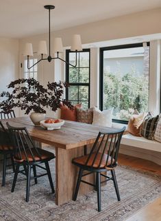 a dining room table with four chairs and a bowl of fruit on it, in front of a window