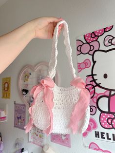 a hello kitty crocheted purse hanging on a wall with pink and white accessories