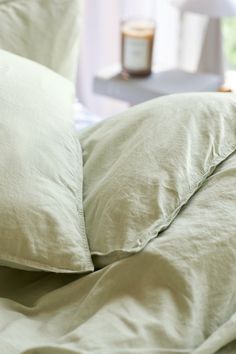 an unmade bed with two pillows and a jar of honey on the table in the background