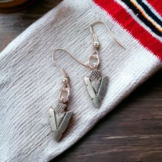 Embrace the spirit with our Southwestern Arrowhead Earrings. These striking earrings feature antique silver finish arrowhead charms with intricate double-sided detailing. With their bold yet elegant design, they add a touch of rugged charm to any outfit.  Southwestern Arrowhead Earrings Charm Style: Fancy Double-sided Arrowhead Overall Length: Just under 1-3/4 inches long (including earwires) Width: Just over 3/8 inch Materials: Lead-free and nickel-free metals Earwire Options: Choose between silver-plated or solid .925 sterling silver Sold by: Pair These earrings are a perfect blend of cultural heritage and contemporary style. They are sold by the pair, offering a unique accessory for those who appreciate distinctive Southwestern aesthetics. Southwestern Arrowhead Earrings - These danglin Arrowhead Earrings, Arrow Jewelry, Earrings Everyday, Southwestern Jewelry, Cultural Heritage, Accessories Unique, Charm Earrings, Solid 925 Sterling Silver, Halloween Shopping