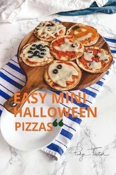 easy mini halloween pizzas on a wooden platter with blue and white striped towel