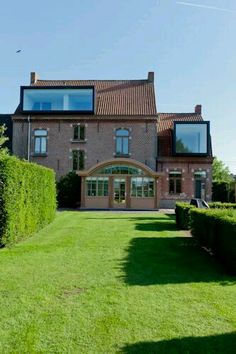 a large brick house sitting on top of a lush green field next to a tall hedge