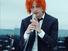 a man with orange hair holding a microphone in front of him and wearing a suit