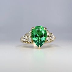 an emerald and diamond ring on a white surface