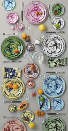 an assortment of plates and utensils are arranged on a table top with fruit