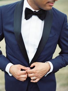 a man in a blue tuxedo with his hands on his chest and wearing a black bow tie