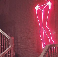 a neon sign on the side of a building next to a stair case and railing