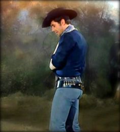 a man dressed in blue is standing with his hands on his hips and wearing a cowboy hat