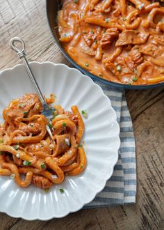 a white plate topped with pasta next to a skillet filled with meat and sauce