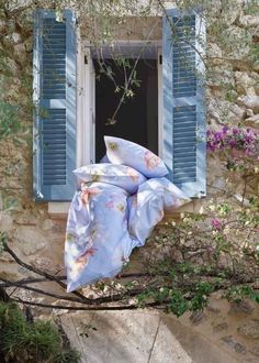 an open window with blue shutters and pillows on it