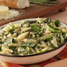 a bowl filled with pasta and spinach on top of a table next to bread