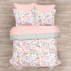 a bed with pink comforter and pillows on top of it in front of a wooden floor