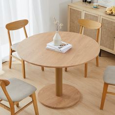 a round wooden table with four chairs around it and a vase on the table top