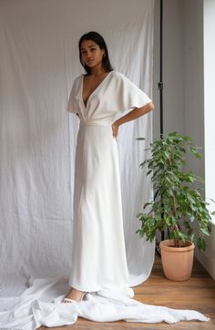 a woman standing in front of a white backdrop wearing a long dress with an asymmetrical neckline