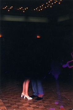 two people standing in the dark with their feet on each other's legs and one person wearing high heels