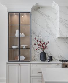 a kitchen with white cabinets and marble counter tops, along with a vase filled with red flowers