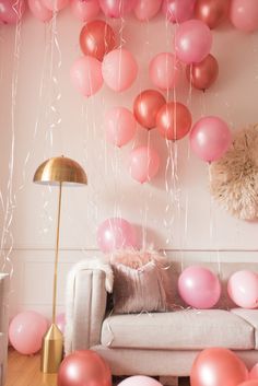 pink and gold balloons are hanging from the ceiling above a couch in a living room