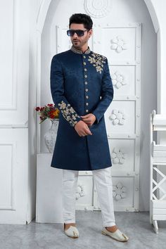 a man in a blue sherwa with white pants and shoes standing next to a wall