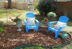 two blue chairs sitting in the middle of a flower bed next to a potted plant