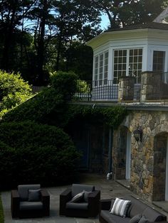 an outdoor living area with couches and chairs in front of a stone building surrounded by greenery