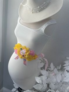 there is a white hat on top of a mannequin's body with flowers around it