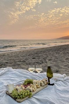 two glasses of wine and cheese on a blanket at the beach