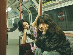 two people sitting on a subway train with their hands up to their ears and looking at the camera