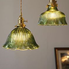 two green glass pendant lights hanging from a ceiling fixture in a room with a framed photograph on the wall