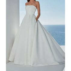 a woman in a white wedding dress standing on a balcony with the ocean behind her