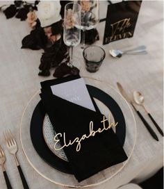 a place setting with black and white plates, silverware and napkins that read elizabeth