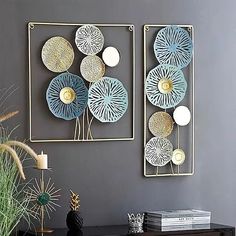 two decorative wall hangings on a gray wall next to a black table and plant