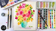 watercolors and paints are sitting on a table with flowers in a vase