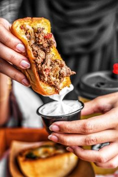 a person holding up a piece of bread with meat on it in a small cup