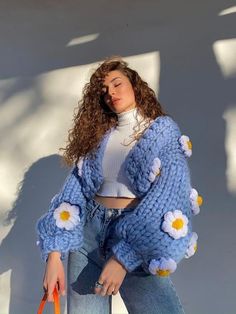 a woman with curly hair is holding an orange handbag and wearing a blue knitted cardigan