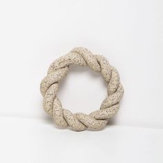 a white rope with black speckles is shown on a white surface and sits in front of a wall