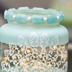 a glass jar that has some lights in it and beads on the lid, sitting on a table