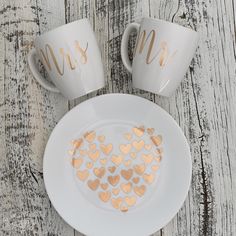 two coffee mugs with gold foil hearts on them next to a plate that says mr and mrs