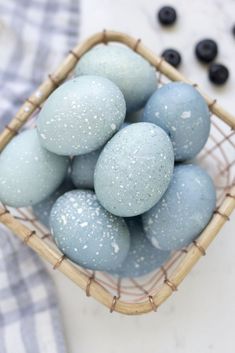 a basket filled with blue dyed eggs on top of a white tablecloth next to black berries