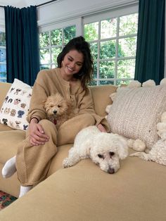 a woman is sitting on a couch with two poodles in front of her