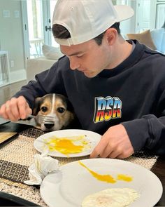 a man sitting at a table with two plates of food in front of him and his dog