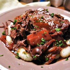 a white plate topped with meat and potatoes covered in gravy on top of a wooden table