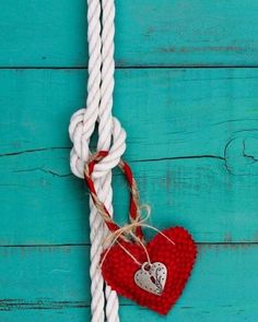 a heart hanging from a rope on a blue wooden background with white and red ropes