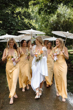 a group of bridesmaids walking in the rain with umbrellas